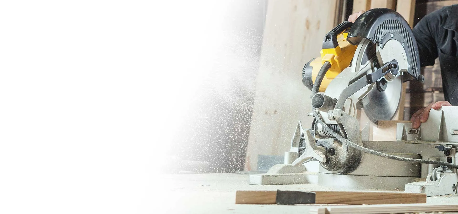 A contractor making a precise cut on a miter saw, sawdust in the light