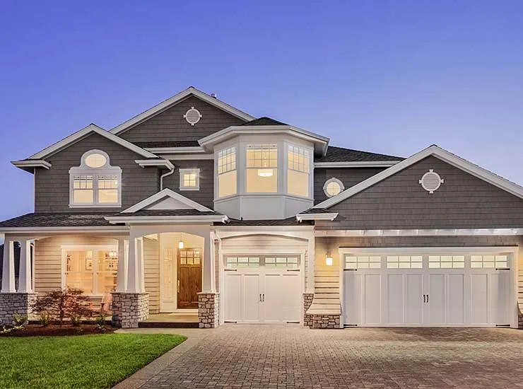 A craftsman-style home at dusk with warm lit windows, shingle roofing and a stone entry